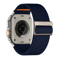 Alternate text: "Back view of a modern smartwatch with a stone-colored case and a white woven nylon band featuring an orange loop, alongside a silver buckle with mountain engraving."