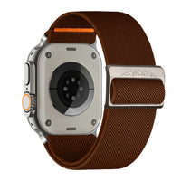 Alternate text: "Back view of a modern smartwatch with a stone-colored case and a white woven nylon band featuring an orange loop, alongside a silver buckle with mountain engraving."